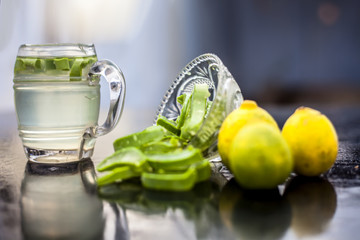 Close up of glass mug on wooden surface containing aloe vera and lemon juice detox drink along with its entire raw ingredients with it. Horizontal shot with blurred background.