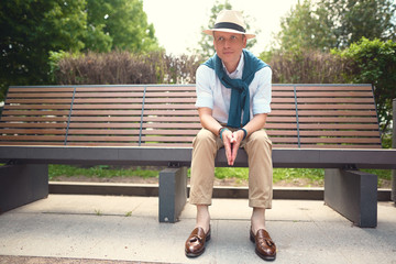 Fototapeta premium Full length portrait of a guy sitting on a bench in a hat 