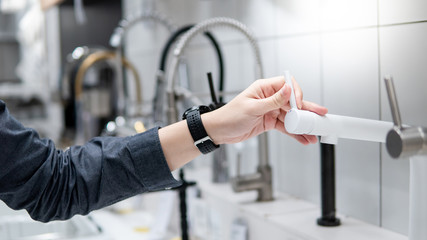 Male hand choosing modern white water tap in furniture store. Home improvement for domestic kitchen.