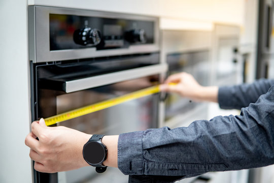 Male Interior Designer Hand Using Tape Measure On Oven In The Kitchen Showroom In Furniture Store. Handy Cooking Appliance On Domestic Kitchen Counter. Home Improvement Concept