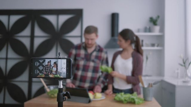 slimming blog, attractive vloggers male and female prepare healthy brunch with vegetables and greens in cuisine while camera cell phone records video for subscribers at social networks