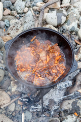 Meat and vegetables are fried in a pilaf cauldron over a fire. Cooking food in nature. National cuisine. Horizontal photo of food. 