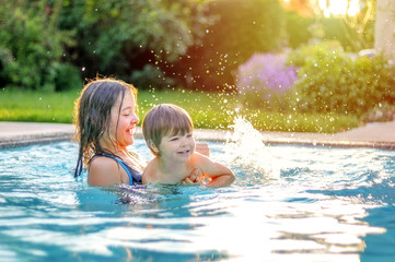 Happy siblings playing in swimming pool outdoors in garden. Preteen sister teaching her little...