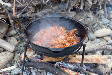 Meat and vegetables are fried in a pilaf cauldron over a fire. Cooking food in nature. National cuisine. Horizontal photo of food. 