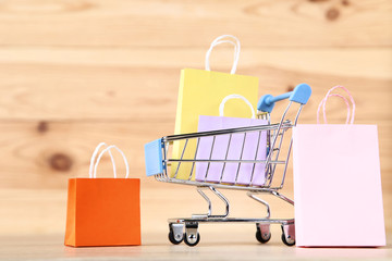 Small metal cart with shopping bags on brown wooden table