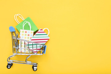 Small metal cart with shopping bags on yellow background
