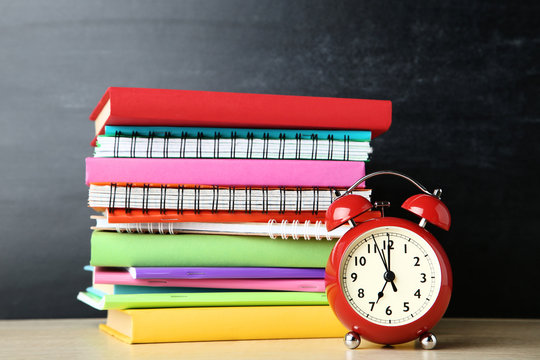 School books and notebooks with alarm clock on blackboard background