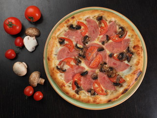 Pizza with ham, tomatoes and mushrooms in a plate