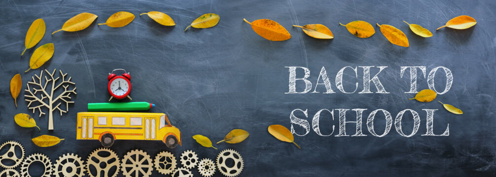 education and back to school concept. Top view photo of cardboard school bus, alarm clock and pencil next to tree with autumn dry leaves over classroom blackboard background