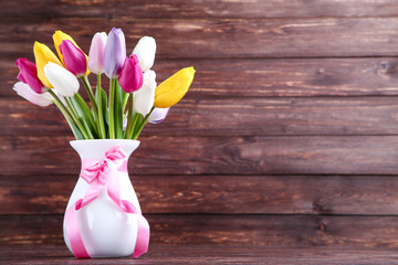 Bouquet of tulip flowers in vase on brown wooden background