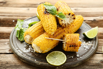 Grilled corn with lime pieces and basil leafs on wooden table