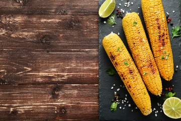 Grilled corn with lime pieces and seasonings on wooden table