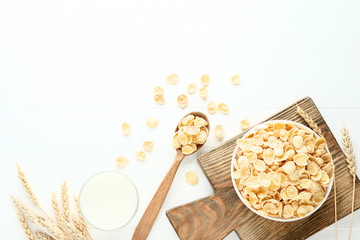 Corn flakes in bowl with wheat ears and glass of milk on wooden table