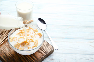 Pouring milk in bowl of corn flakes on wooden table