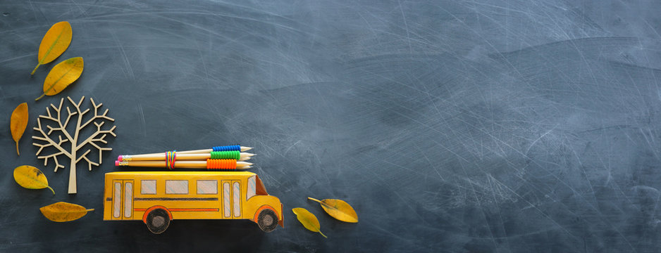 education and back to school concept. Top view photo of cardboard school bus and pencils next to tree with autumn dry leaves over classroom blackboard background