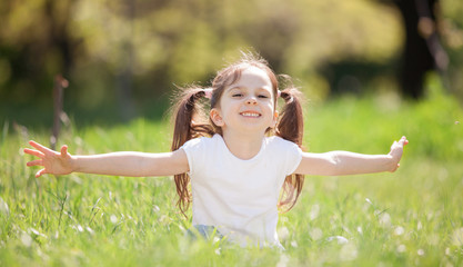 Naklejka na ściany i meble Fun little girl play in the park. Beauty nature scene with colorful background at summer or spring season. Family outdoor lifestyle. Happy girl relax on green grass