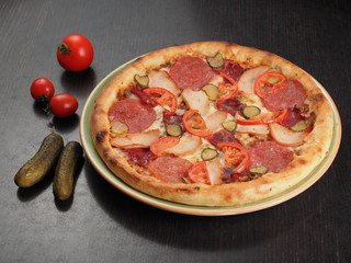 Pizza with salami, chicken, tomatoes and pickled cucumbers on a plate