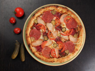 Pizza with salami, chicken, tomatoes and pickled cucumbers on a plate