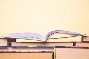 Open book is on stack of other books on a pastel yellow background. The concept of learning, education, reading, libraries, the beginning of the school year, the acquisition of knowledge. Copy space.