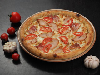 Pizza with ham, chicken, tomatoes and cheese on a plate