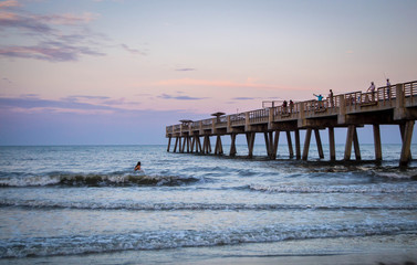 Fototapeta premium People surfing by pier in the sunset