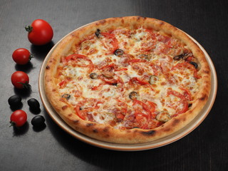 Pizza with sausage, olives, tomatoes and pickled cucumbers on a plate