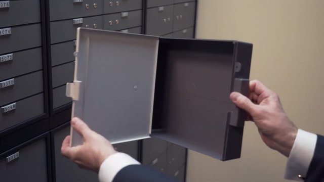 Bank clerk in suit shows empty safe security depository plastic cell container to client in winter jacket