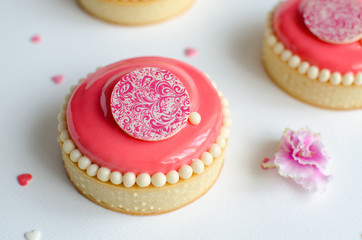 Mousse mini tarts covered with pink glaze and decorated with chocolate elements on white background