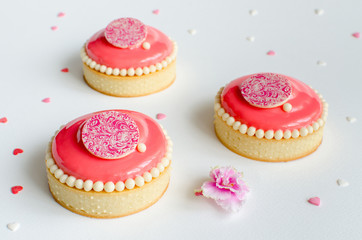 Mousse mini tarts covered with pink glaze and decorated with chocolate elements on white background