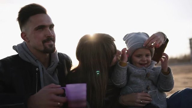 Lifestyle portrait mom, dad and child in happines at the outside on the beach against sun shine. Young, stylish family outdoors together, mother make fun with son