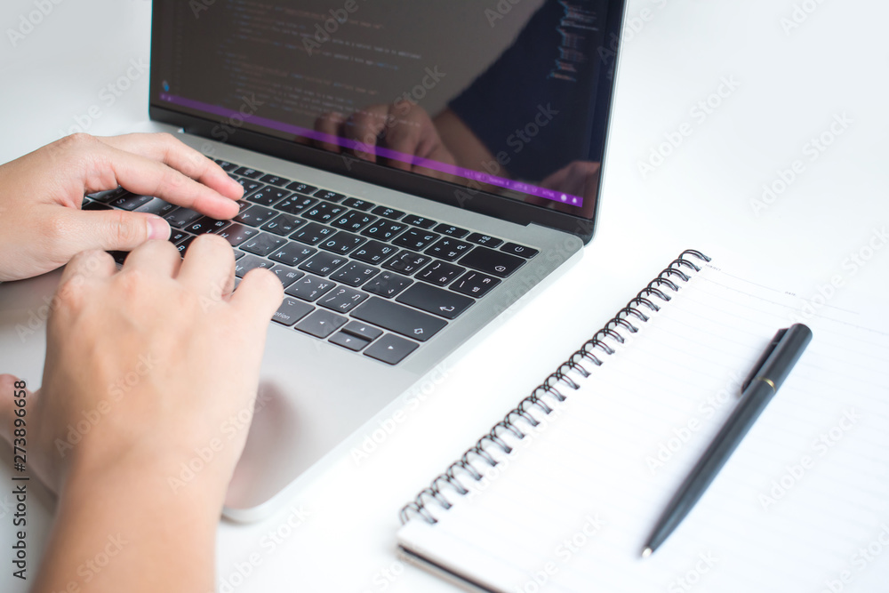 Poster close up to the programmer's hand, work seriously on modern white work desks. with a note book on th