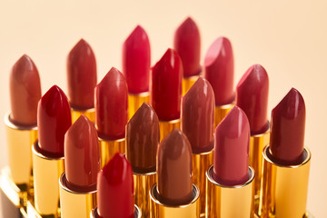 close up of various red shades of lipstick in tubes isolated on beige