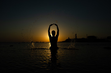 Silhouette of young girl in the water that splashing their hair against sunset