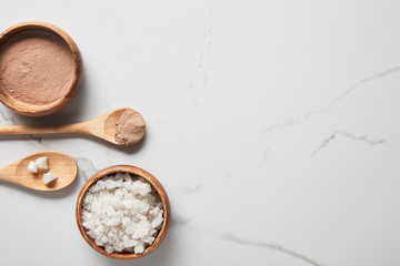top view of clay powder and sea salt in wooden bowls and spoons on marble table
