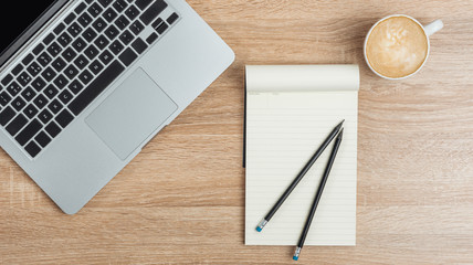 Laptop, open notebook with pencils and a cup of coffee on the desktop. View from above.