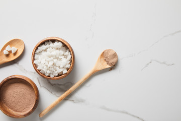 top view of clay powder and sea salt in bowls on marble table near wooden spoons