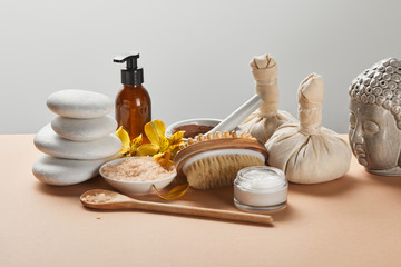 spa cosmetics, stones, massage brush, candle, Buddha figurine and yellow flowers on beige surface...