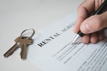 Hand is writing with a pen on a rental agreement document, house keys in the background