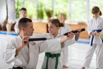Dark-haired aikido trainer helping girl to use nunchucks