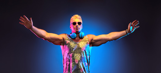 Fashion Charismatic DJ man in Stylish headphones, trendy hairstyle in neon creative light with hands up. Nightlife club, house music concept. Handsome sexy muscular guy enjoy music dancing, bunner