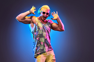 Fashion Excited Muscular DJ man dance music, colorful neon light. Handsome pumped-up blonde...