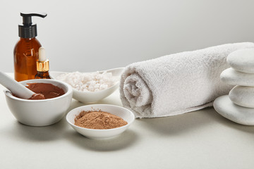 sea salt and clay in bowls, cotton towel, stones, bottles on white surface isolated on grey