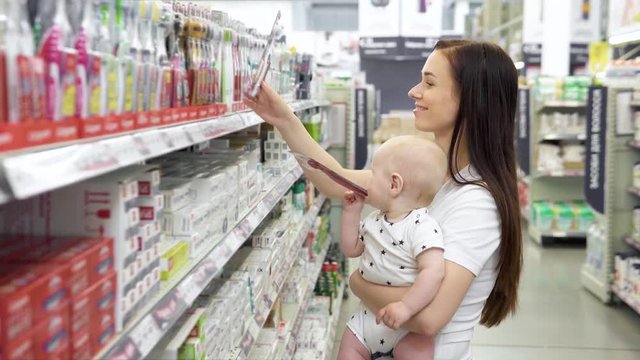 Beautiful woman with baby son shopping in supermarket, young Mother chooses toothbrushes for their family in the market