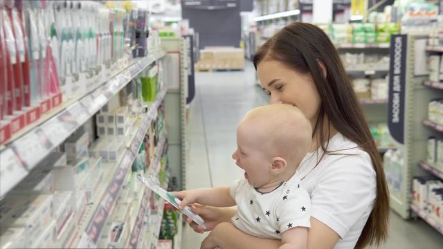 Beautiful woman with baby son shopping in supermarket, young Mother chooses toothpaste for their family in the market