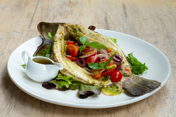 close up of baked sea bass fish mediterranean style with cherry tomatoes, olives, capers and basil
