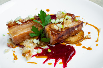 close up of crispy slow cooked pork belly in beetroot sauce and apple