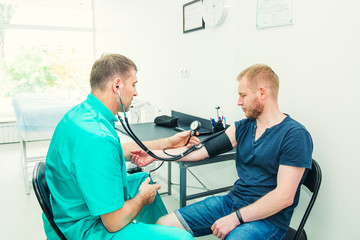 Male Doctor using sphygmomanometer with stethoscope checking blood pressure to a young male patient...