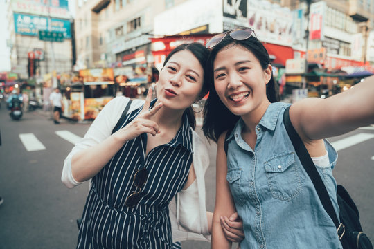 Friends having fun outdoors. two asian girls travelers with sunglasses standing on street by zebra cross making self portrait. cute women tourists taking selfie on city urban road taiwan taipei