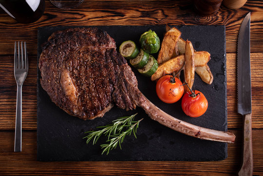 grilled tomahawk ribeye steak on black stone plate