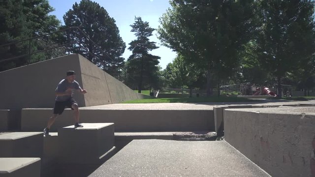 Male parkour athlete in backwards hat performs acrobatic side flip onto concrete ledge. Shot on Sony FS700 slow motion 240 fps